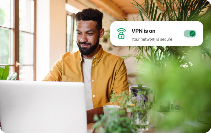 Un hombre rodeado de plantas sonríe frente a una computadora portátil